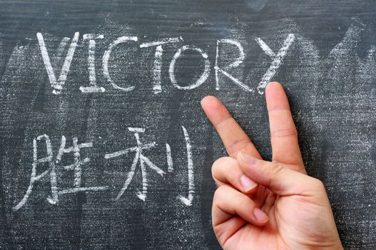 Victory - word written on a blackboard with a Chinese translation, with a hand gesture