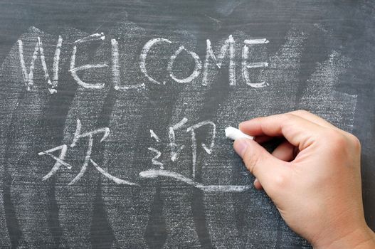 Welcome - word written on a blackboard with a Chinese translation, with a hand holding chalk