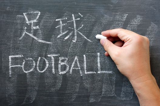 Football - word written on a blackboard with a Chinese version, with a hand holding chalk