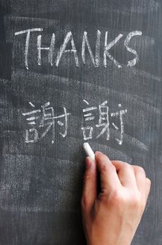 Thanks - word written on a blackboard with Chinese version characters, with a hand holding chalk.