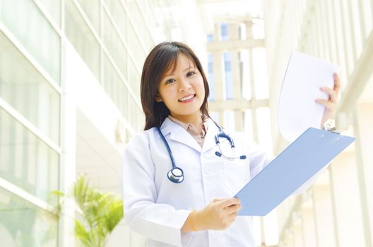 Young female practitioner doctor holding a writing pad standing inside hospital