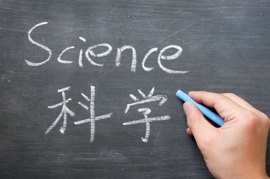 Science - word written on a smudged blackboard with a Chinese translation,with a hand holding chalk