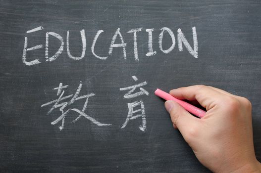 Education - word written on a smudged blackboard with a Chinese translation,with a hand holding chalk