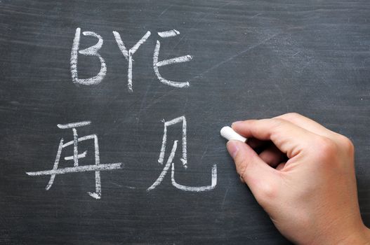 Bye- word written on a smudged blackboard with a Chinese translation, with a hand holding chalk