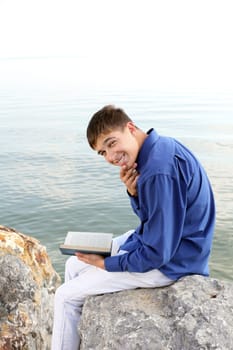 happy teenager sitting with a book on the stone on the seaside