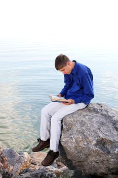 happy teenager sitting with a book on the stone on the seaside