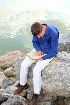 teenager sitting with a book near the water