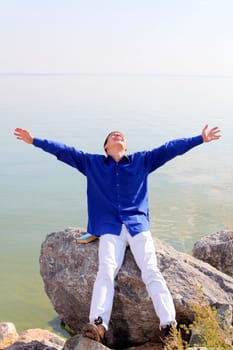 happy young man with hands up on the seaside background in the sunny day