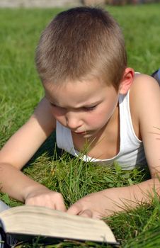 The child attentively reads the book on a summer meadow