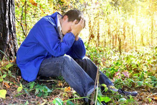 sad teenager sitting in the autumn forest alone