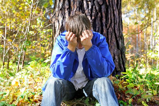 sorrowful teenager sitting in the autumn forest alone