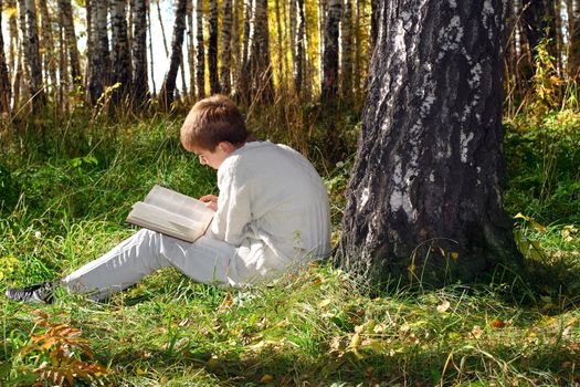 teenage boy sit in autumn forest with a book