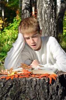 teenage boy sit in autumn forest with a book