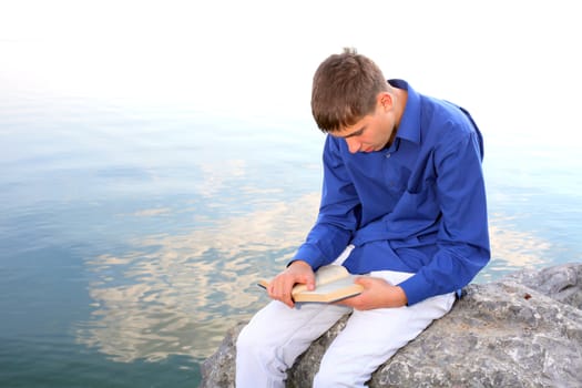 teenager sitting with a book near the water