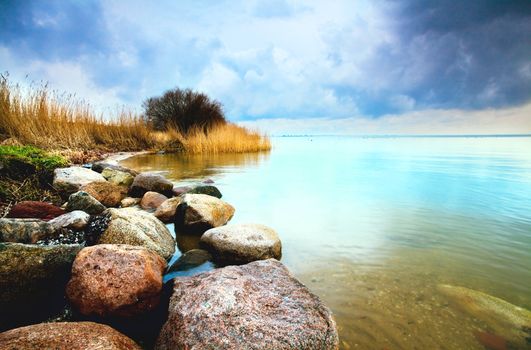 colorful view on the big lake with stones and clouds on sky