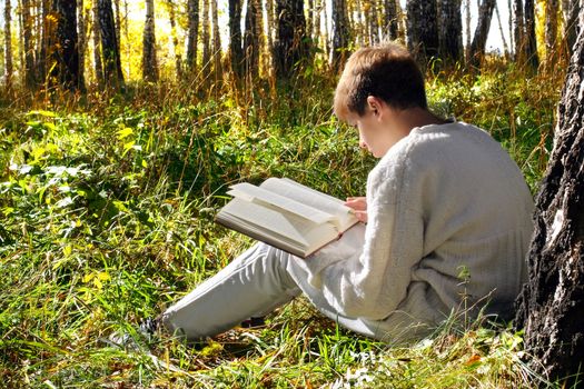 teenage boy sit in autumn forest with a book