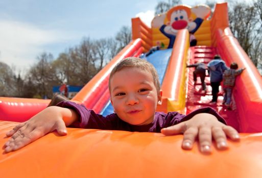 Smiling little boy playing on inflatable slide, looking at camera
