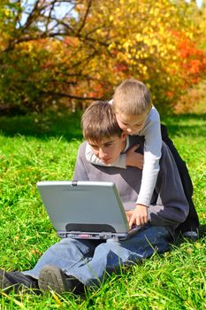 teenager and kid with laptop on the meadow