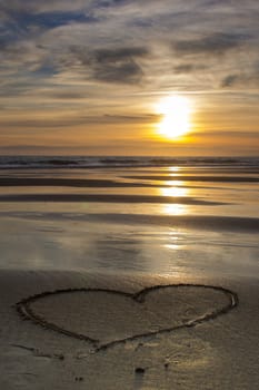 heart drawn in the wet sand on the beach at sunset