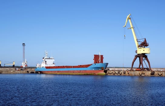 The cargoship and the crane on a background of the blue sky