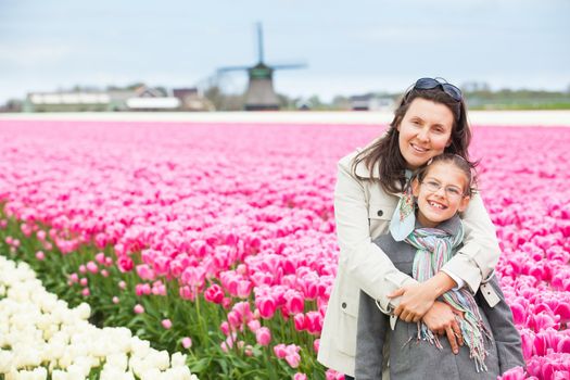 Girl with her mother walks between of the purple tulips field