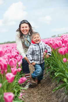 Boy with mother runs between of the purple tulips field