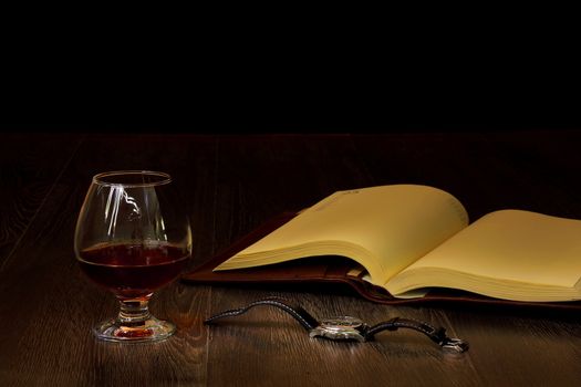 A glass with cognac, cigar and an old book nearby