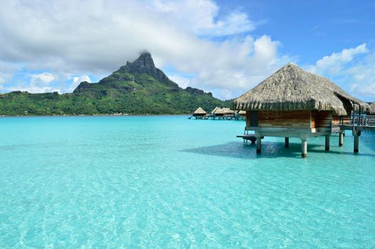 Luxury overwater bungalow in a vacation resort in the clear blue lagoon with a view on the tropical island of Bora Bora, near Tahiti, in French Polynesia.