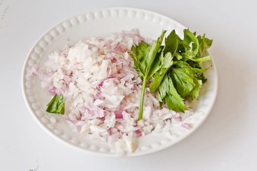Chopped onions and raw parsley on a white plate ready to be cooked