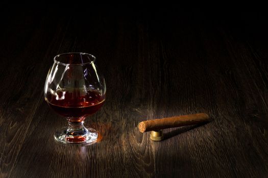 A glass with cognac, cigar and an old book nearby