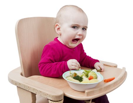 young child in red shirt eating vegetables in wooden chair.