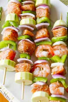 Salmon cubes and Shrimp complimented with vegetables on skewers. Ready to cook. Red onions, zuccini and green peppers.