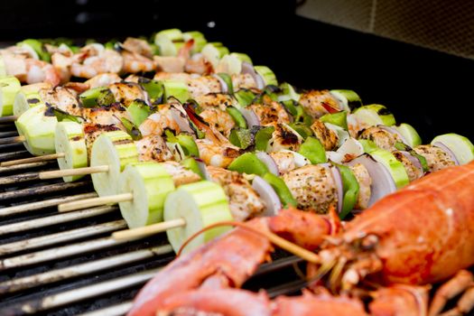 Salmon and Vegetable Skewers and Lobster are on the barbecue.