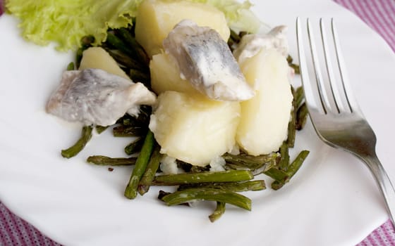 Appetizing marinaded herring with a boiled potato and fried stalks of garlic