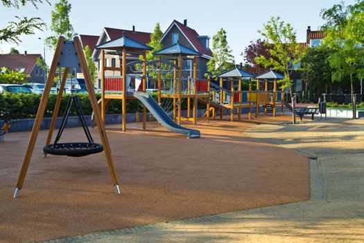 Public playground with colorful wooden climbing construction, swing, slides and rubber floor for safe playing