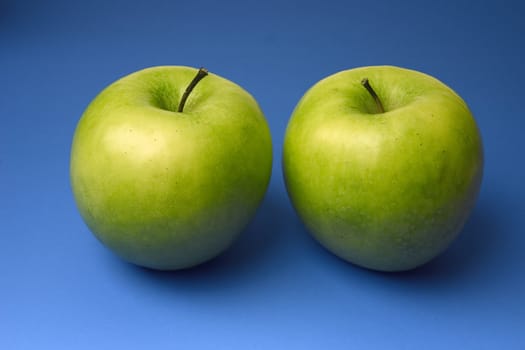 two appetizing apples of green color on a blue background