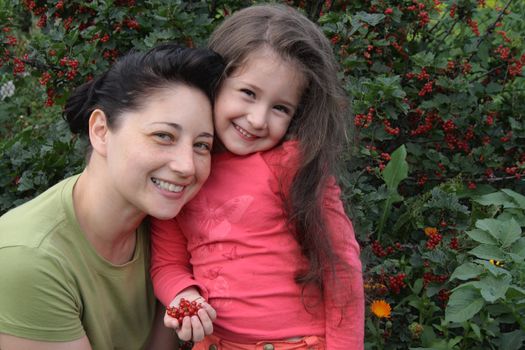 Mum with the daughter on a background of a bush of a red currant