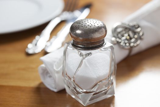 Crystal salt shaker with silver top and set table in background
