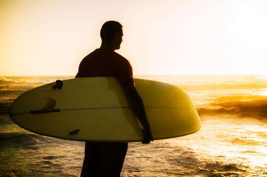 A surfer watching the waves at sunset in Portugal.