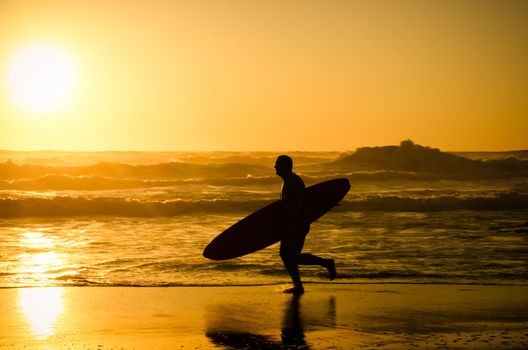 Surfer running on the beach with the waves at sunset in Portugal.