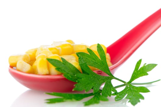 Canned corn in a red ceramic spoon on white  reflective background.