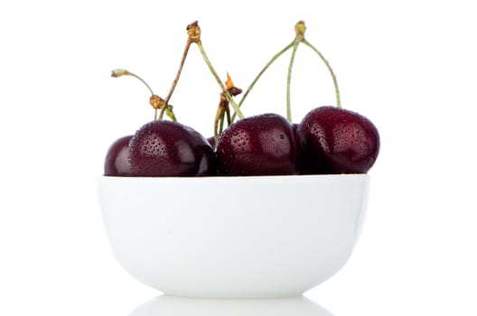 Cherry in white bowl on white reflective background.