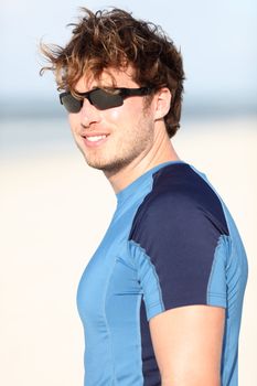 Sporty young man on beach smiling happy after outdoor running workout. Caucasian male fitness model outside.