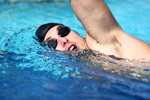 Man swimming crawl. Male freestyle swimmer crawling doing crawl-swimming stroke in pool wearing swimming goggles and swim cap. Caucasian male sport fitness model.