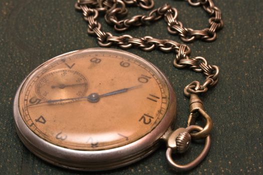 Very old clock with chain lying on rough green  surface - shallow depth of field