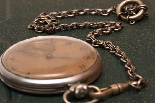 Very old clock with chain lying on rough green  surface - shallow depth of field