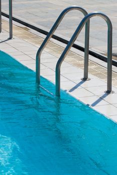 Metal ladder to swimming pool with blue water