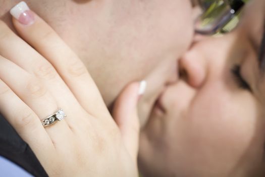 Young Female Hand with Engagement Ring Touching Fiance's Face as They Kiss with Selective Focus on the Ring.
