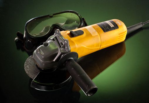 yellow angle grinder with protective glass over green background