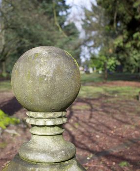 Old weatherd moss covered stone ball sculture with a background of a lawn and trees